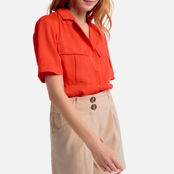Woman wearing orange tailored shirt with cream shorts.jpg