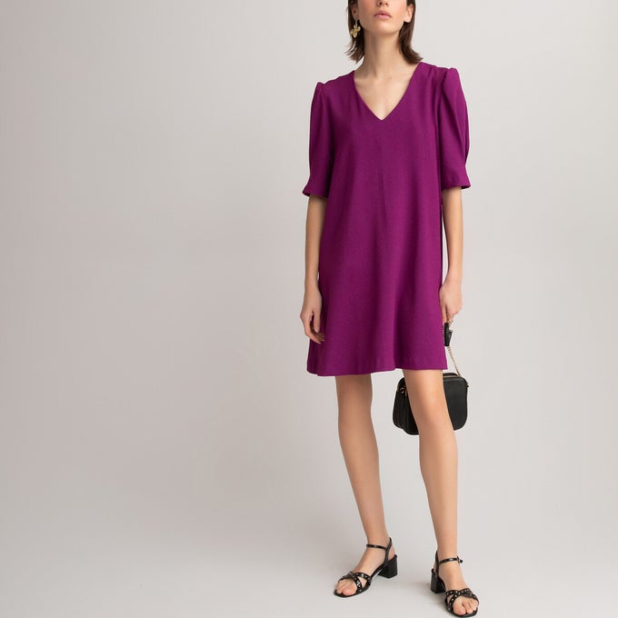 Close up of woman wearing purple v-neck dress with black heels and handbag