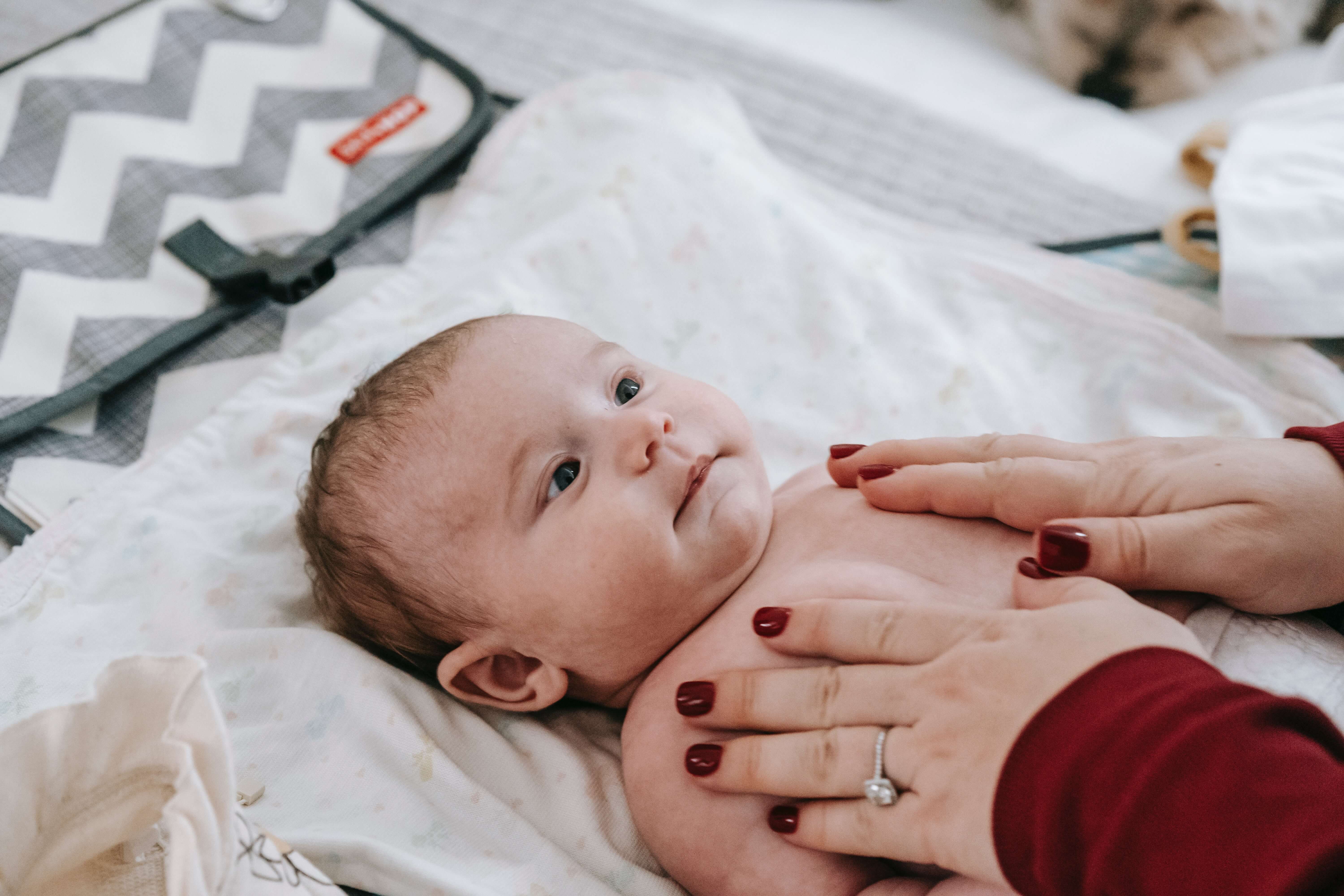 newborn-baby-looking-up-on-changing-mat-mum-holding-him.jpg
