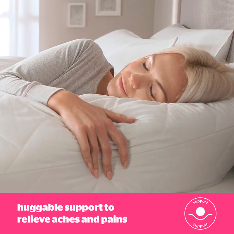 Woman cuddling a large pillow in bed, suggesting soft sleep support
