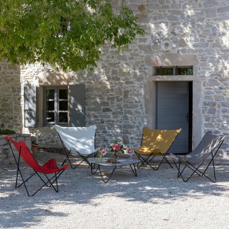 Quatre fauteuils butterfly color&eacute;s autour d&rsquo;une table, devant une maison en pierre
