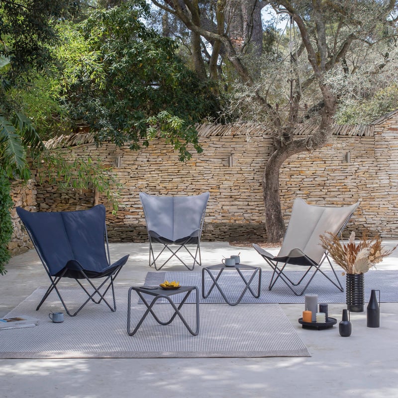 Trois fauteuils butterfly design sur terrasse, autour de tables basses.
